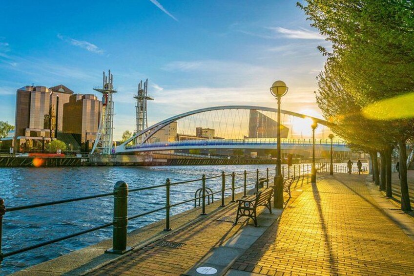 A riverside walkway with a bridge, benches, and lamp posts. 1