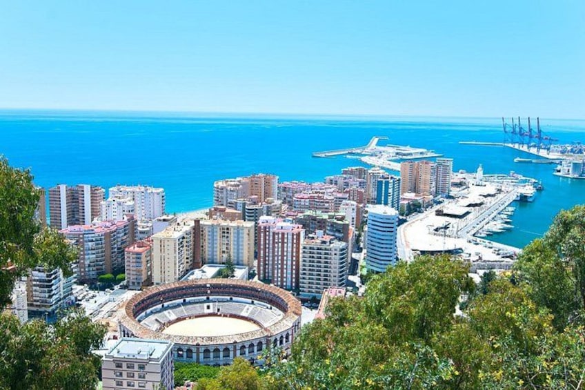 A coastal cityscape with a prominent bullring, high-rise buildings, and a marina. 3