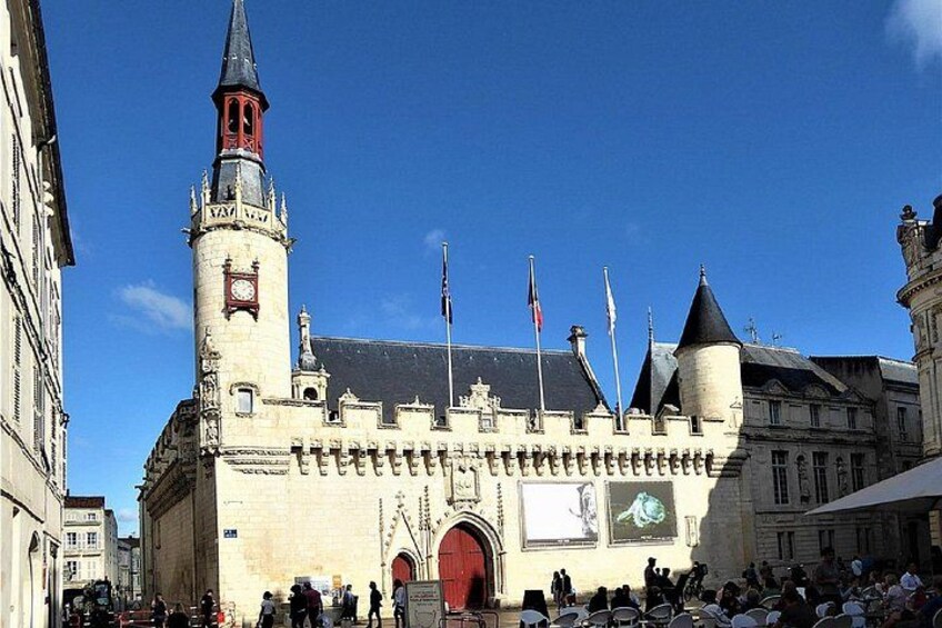 A historic building with a clock tower, flags, and a crowd in front. 5
