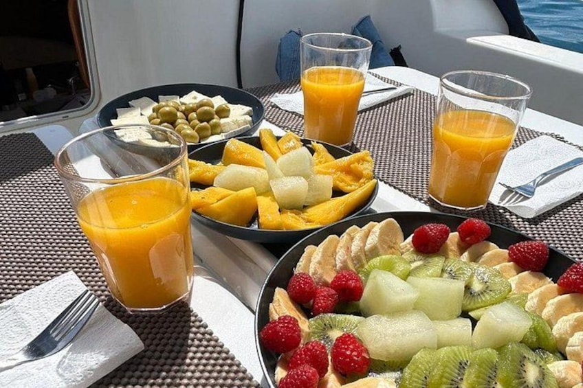 A table with plates of fruit, glasses of orange juice, and a fork on a boat. 5