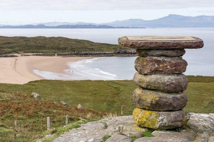 A stack of stones on a grassy hill overlooking a beach. 4