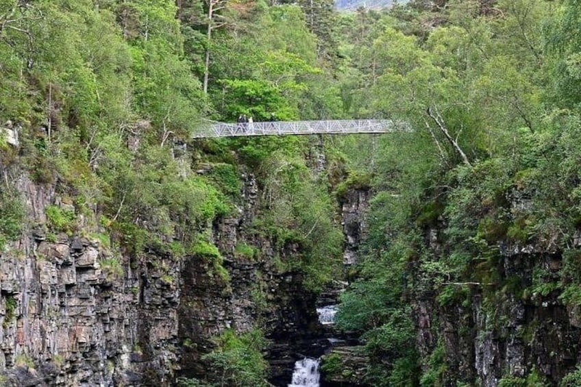 A bridge over a waterfall surrounded by dense forest. 2