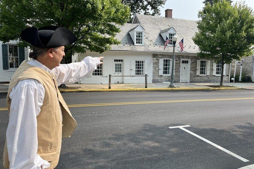 A person in historical costume pointing towards a building with American flags. 2