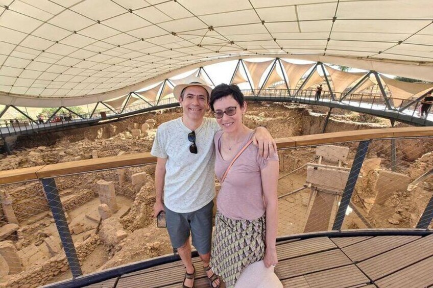 Two people standing on a wooden platform overlooking an archaeological excavation site. 2
