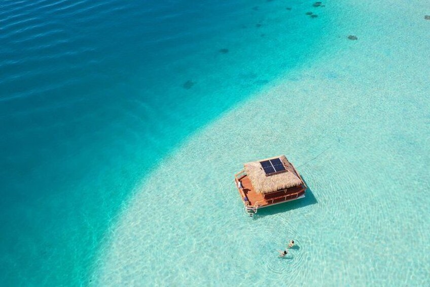 Eine reetgedeckte Hütte an einem klaren, türkisblauen Strand mit flachem Wasser. 1
