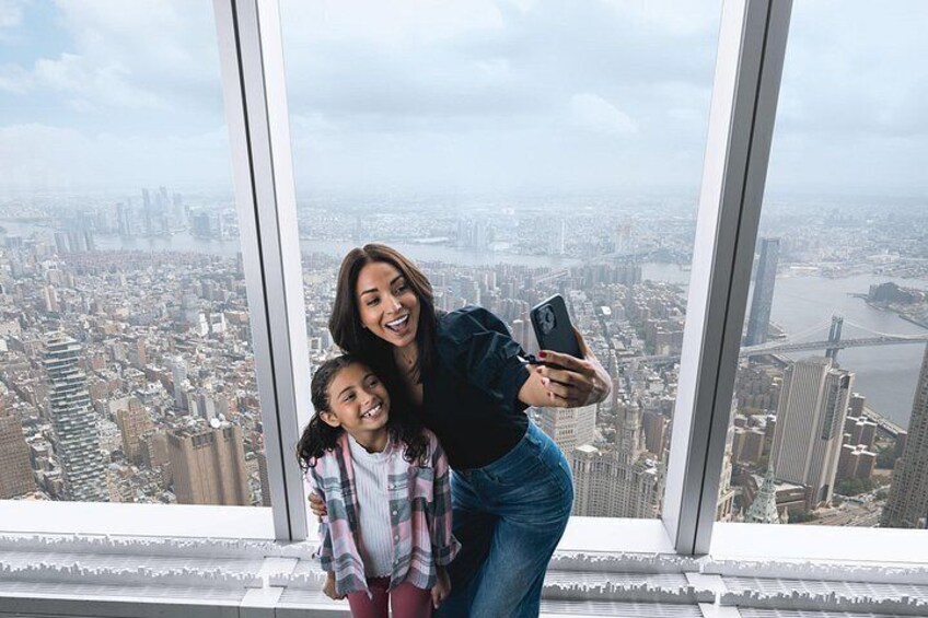 A person taking a selfie with a cityscape view through a large window. 2