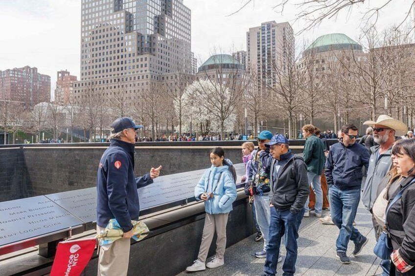 A memorial wall with inscriptions, a crowd of people, and a cityscape with buildings in the background. 4
