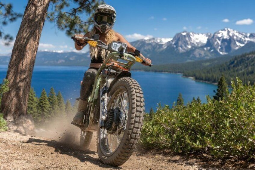 A person riding a dirt bike on a trail with a lake and mountains in the background. 1