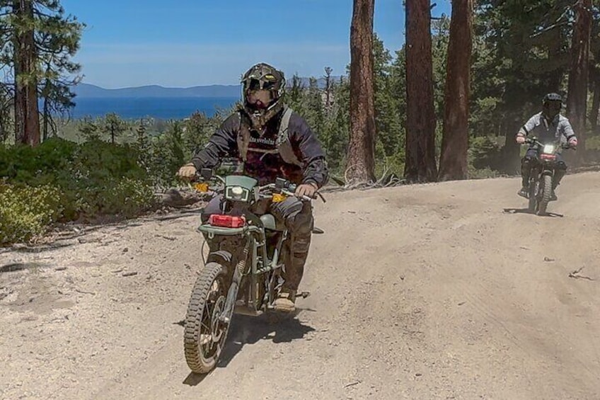 Dos motociclistas en un camino de tierra rodeado de árboles y montañas. 2