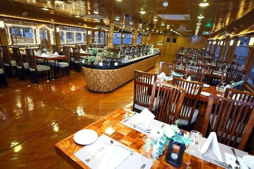 A restaurant with wooden flooring, tables set with white tablecloths, and a central bar area. 4
