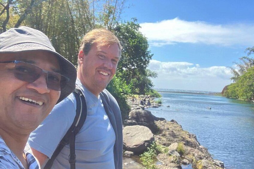 Two people standing by a river with rocks and trees in the background. 4