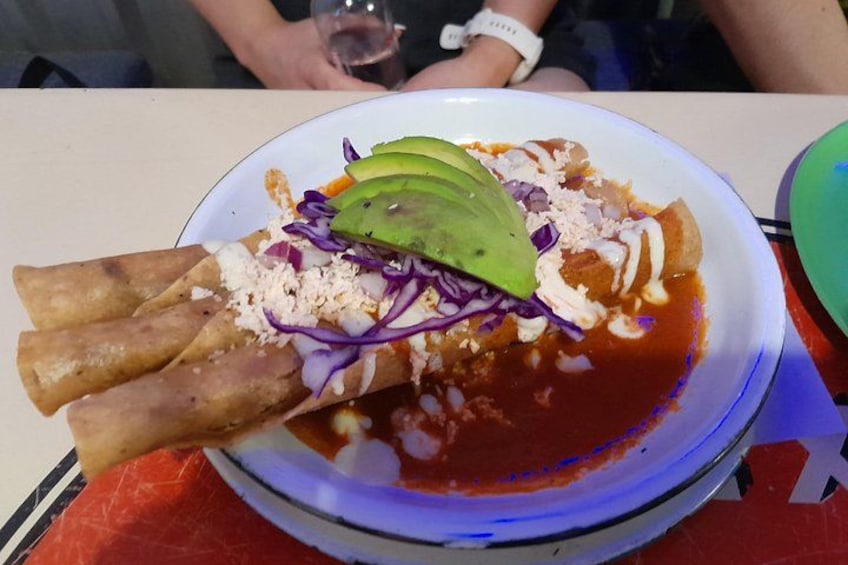 A plate of food with three rolled items, a slice of avocado, shredded purple cabbage, and a red sauce. 4