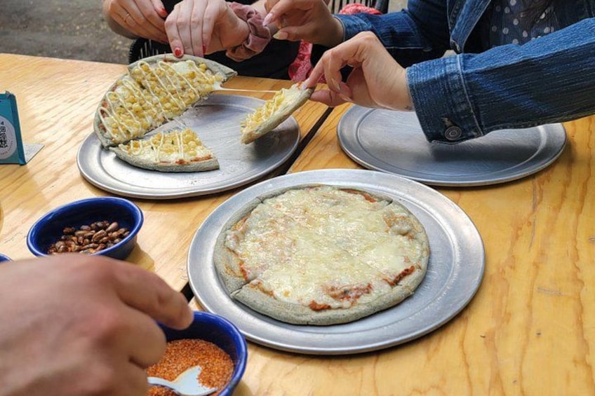 A pizza being sliced and served at a table with bowls of spices. 2