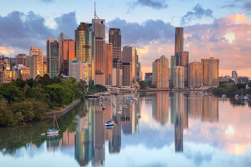 A city skyline with tall buildings, a calm river reflecting the structures, and boats anchored near the shore. 1