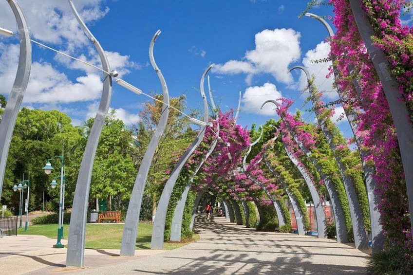 A pathway lined with tall, curved metal structures and flowering trees. 2