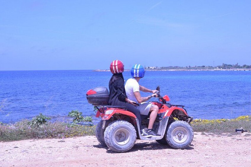 A person riding a red ATV on a dirt path by the sea. 3