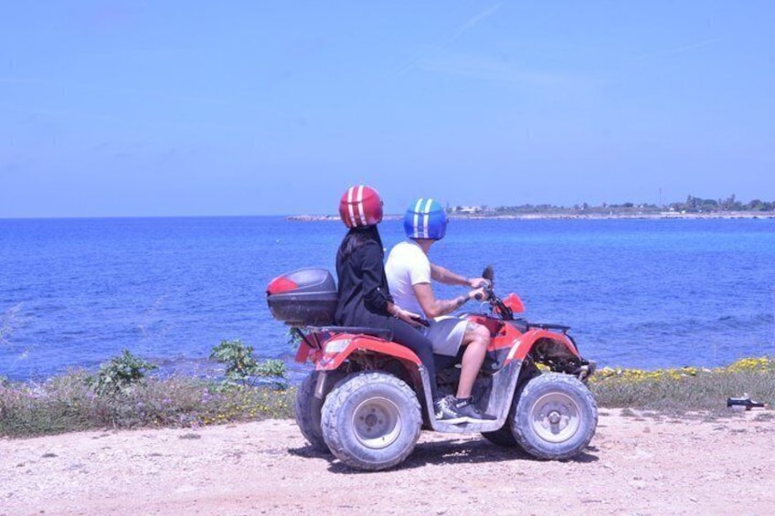 A person riding a red ATV along a dirt path by the sea. 3