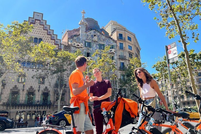Tres personas de pie al aire libre, con bicicletas y un edificio al fondo. 3