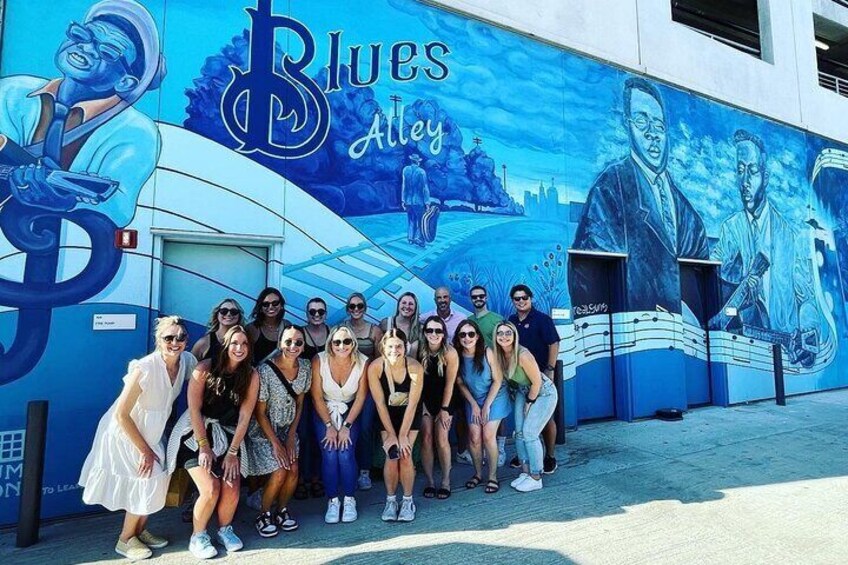 Ein Wandgemälde mit der Aufschrift "Blues Alley" und eine Gruppe von Menschen, die davor posieren. 1