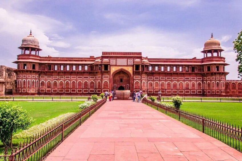A large, red-walled building with domes and arched windows, surrounded by a well-maintained lawn and a paved walkway. 2