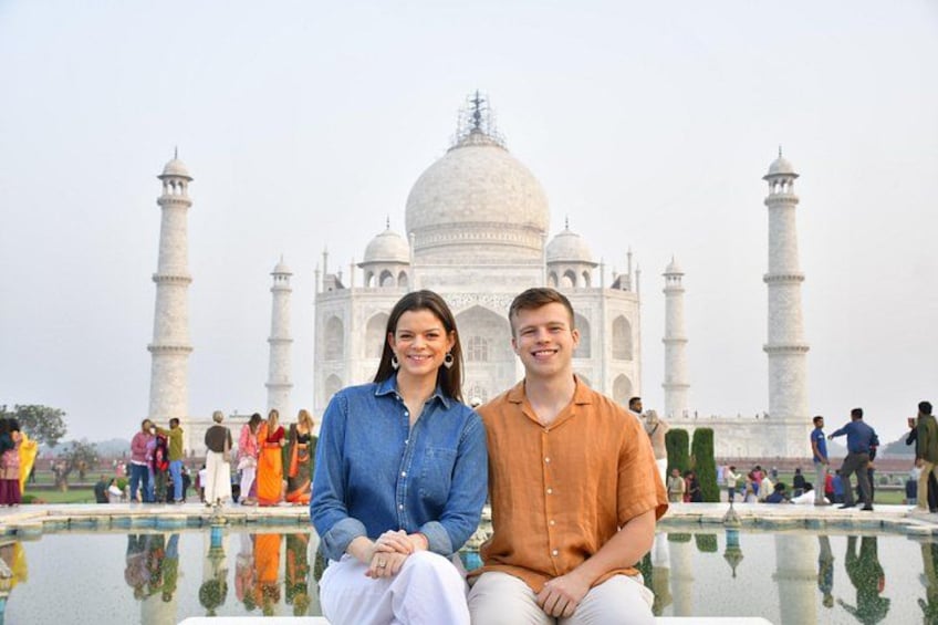 Two people sitting in front of the Taj Mahal with its reflection in the water. 1