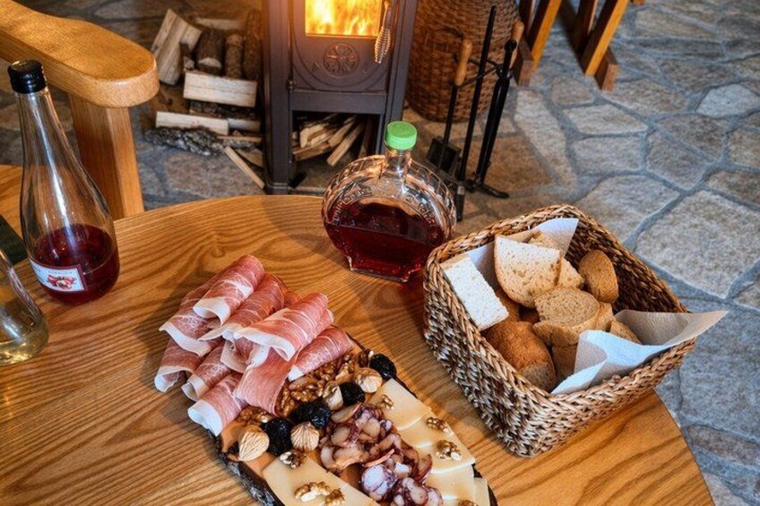 A wooden table with a charcuterie board, a basket of bread, and bottles of red wine. 3