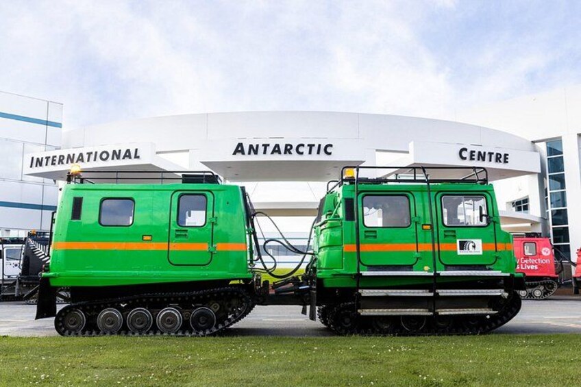 Twee groene rupsvoertuigen geparkeerd voor een gebouw met de tekst 'International Antarctic Centre'. 1
