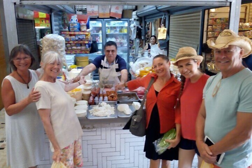 A group of people at a food stall with various food items displayed. 1