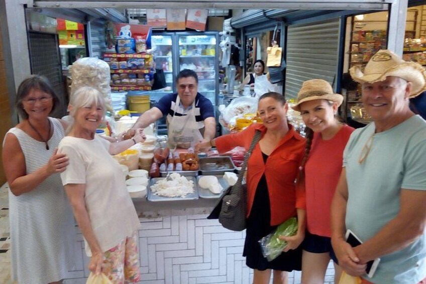 A group of people at a food stall with various food items and a person preparing food in the background. 2