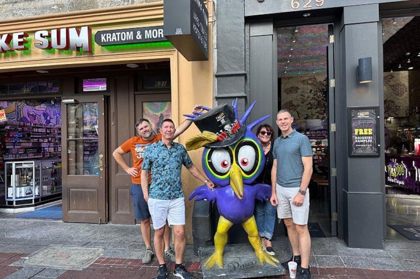 A person in a colorful costume standing in front of a store named 'Kratom & Mor'. 3