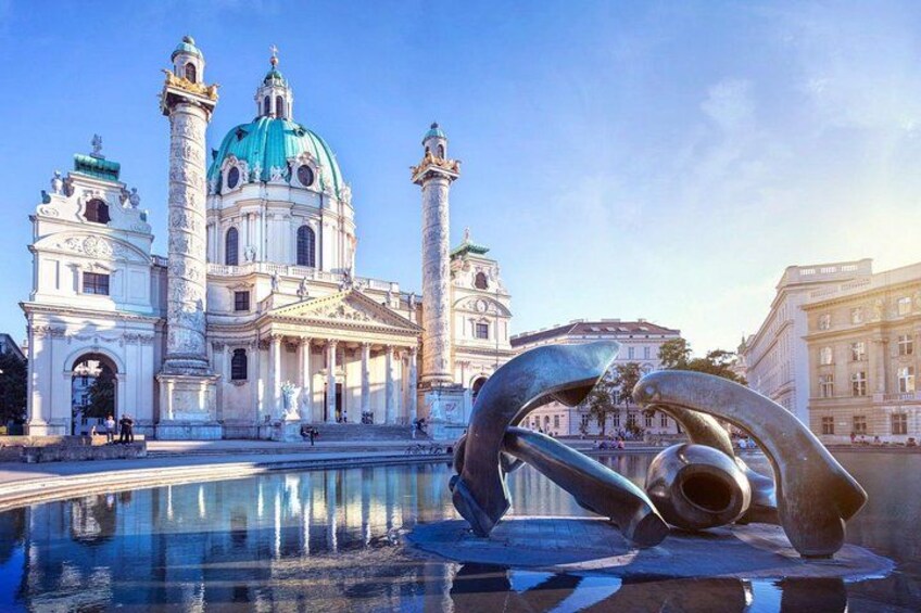 A historic building with a dome and two towers, a reflective water surface, and a modern sculpture. 3