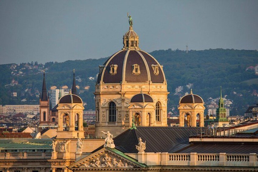 A large domed building with two smaller domes, surrounded by other buildings and a hilly landscape in the background. 2