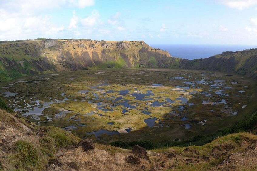 A vast landscape with a large crater, scattered ponds, and steep cliffs. 5