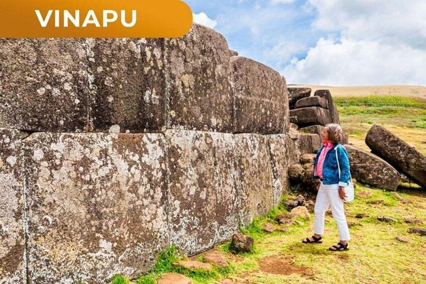 A person standing next to a large stone structure in a grassy field with a clear sky. 3