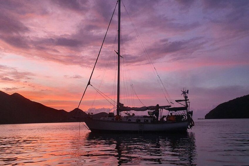 A sailboat on calm water during sunset with mountains in the background. 1