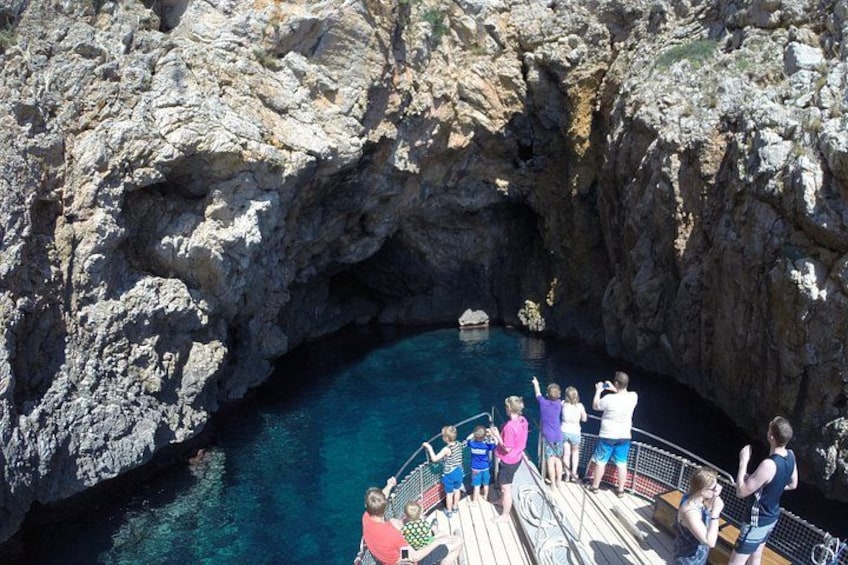 Un groupe de personnes se trouve sur un bateau, près de l’entrée d’une grotte rocheuse, dans une zone où l’eau est d’un bleu cristallin. 2