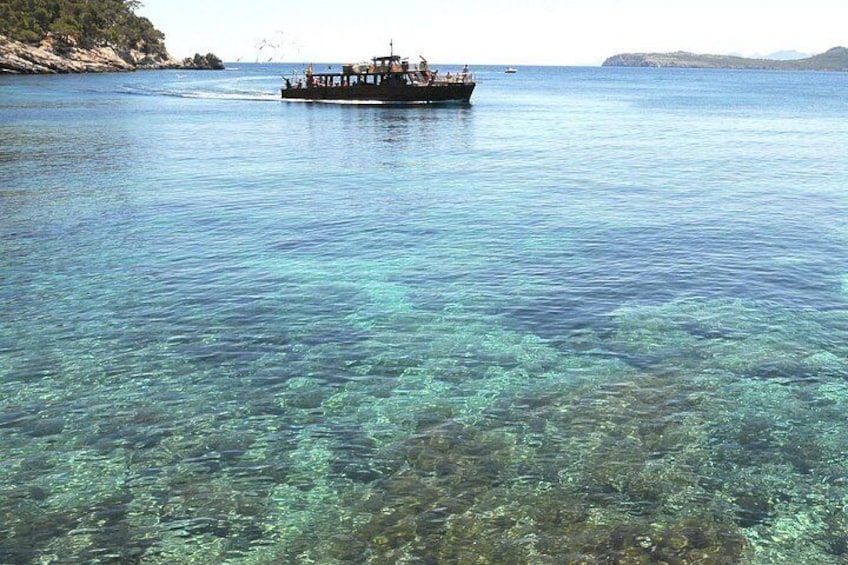 A boat on clear blue water with rocky coastline in the background. 3