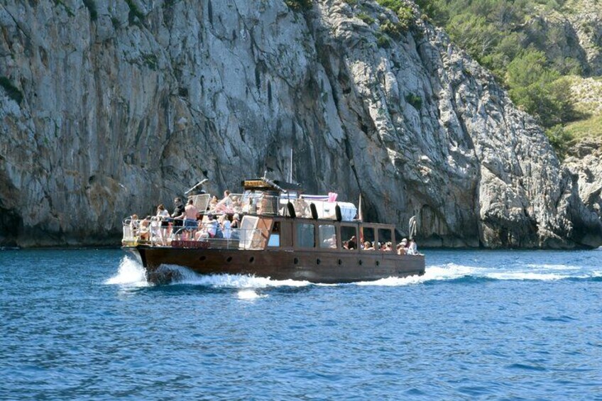 A boat with passengers, rocky cliffs, and clear blue water. 5