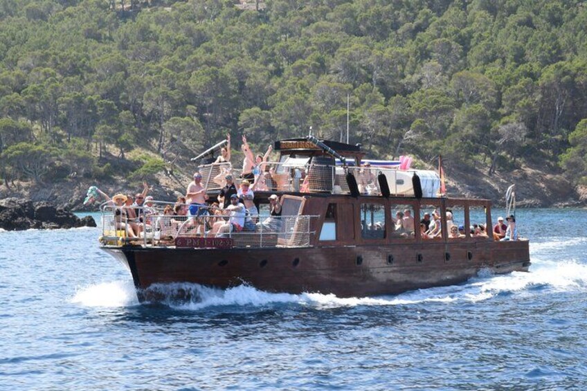 A boat with people on it, moving through water with a forested coastline in the background. 4