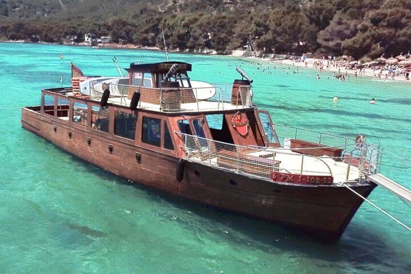 A wooden boat on turquoise water with a beach and trees in the background. 1