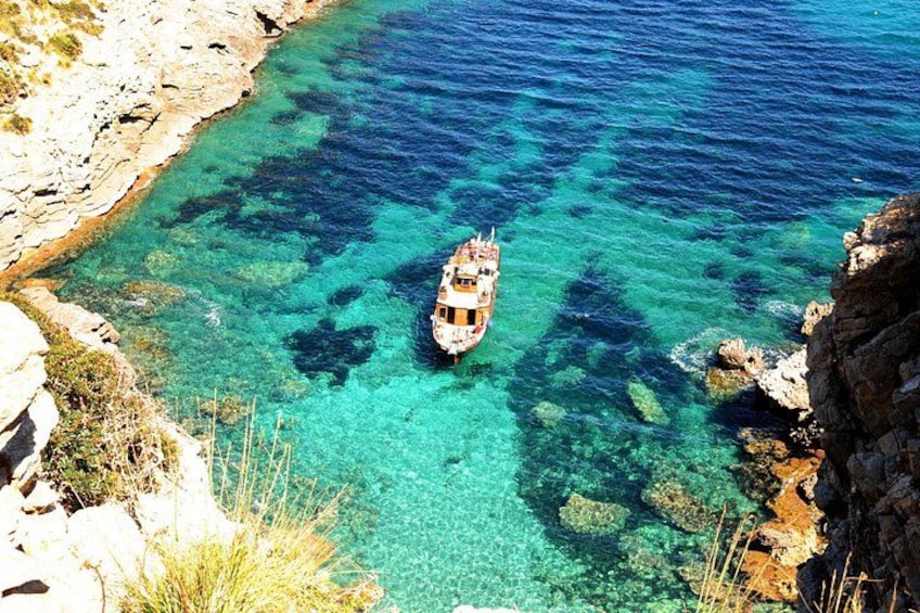 Een boot in helder turquoise water nabij rotsachtige kliffen. 3