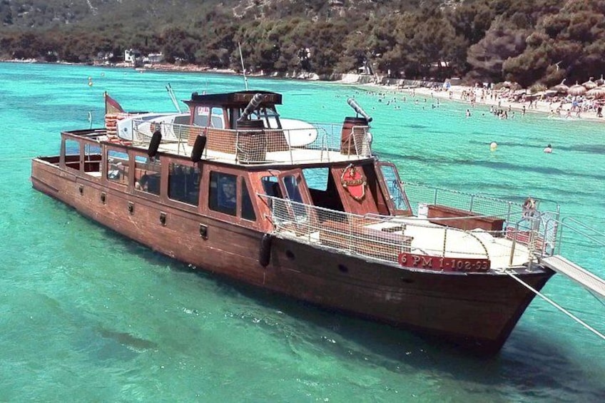 Un bateau en bois sur une eau turquoise, avec une plage et des arbres en arrière-plan. 1