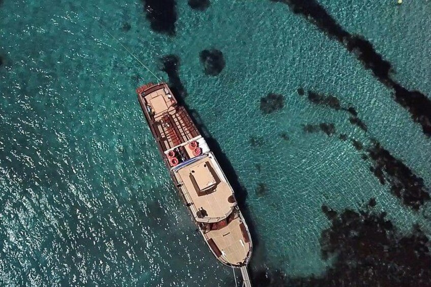 Luchtbeeld van een schip dat in helder turquoise water ligt ankeren, met zichtbare structuren onder water. 5
