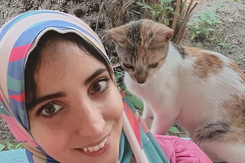 A person wearing a striped headscarf and a pink garment, with a cat in the background. 5
