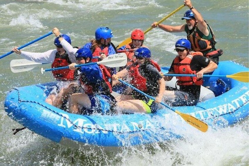 A group of people in a blue inflatable raft on a river, wearing helmets and life jackets. 1
