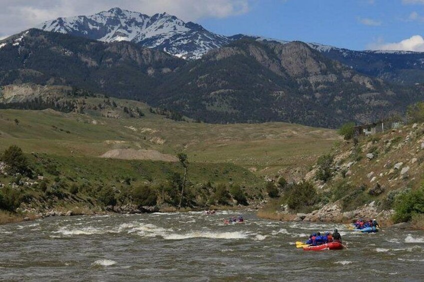 A river with rapids, a group of people rafting, and snow-capped mountains in the background. 2