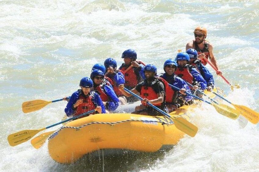 A group of people in a yellow raft with blue helmets and life jackets, paddling through rough water. 5