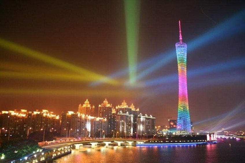 Ein hell erleuchteter Turm mit Regenbogenfarben, umgeben von einer Skyline mit beleuchteten Gebäuden. 2