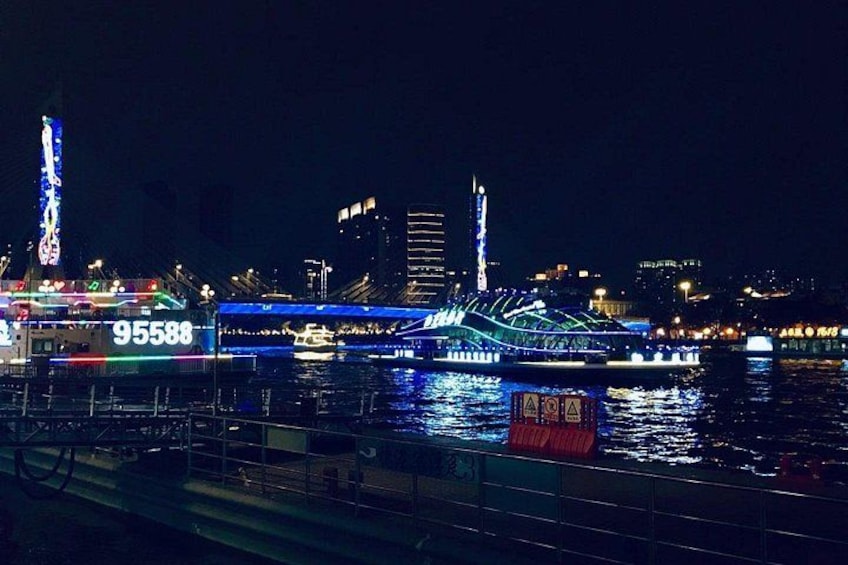 Ein hell beleuchtetes Flussboot mit der Nummer 95588, liegt an einem Steg vor einer Stadtkulisse. 1