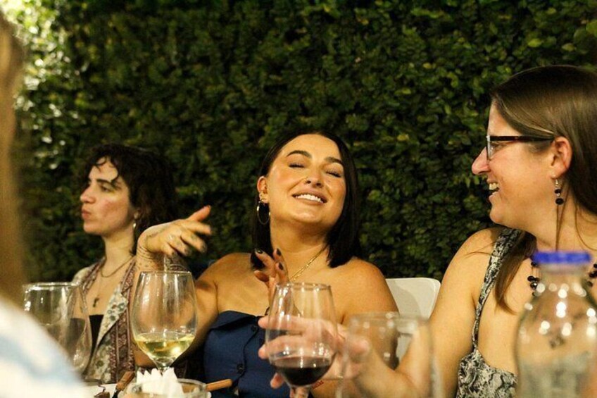 Un groupe de personnes réunies lors d’un événement social, tenant des verres à vin, avec un arrière-plan verdoyant et feuillu. 2